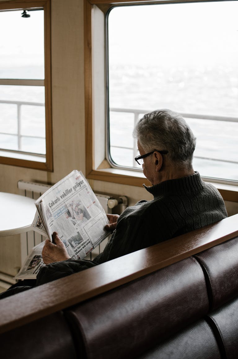 Elderly man reading newspaper inside ferry, enjoying a peaceful travel moment.