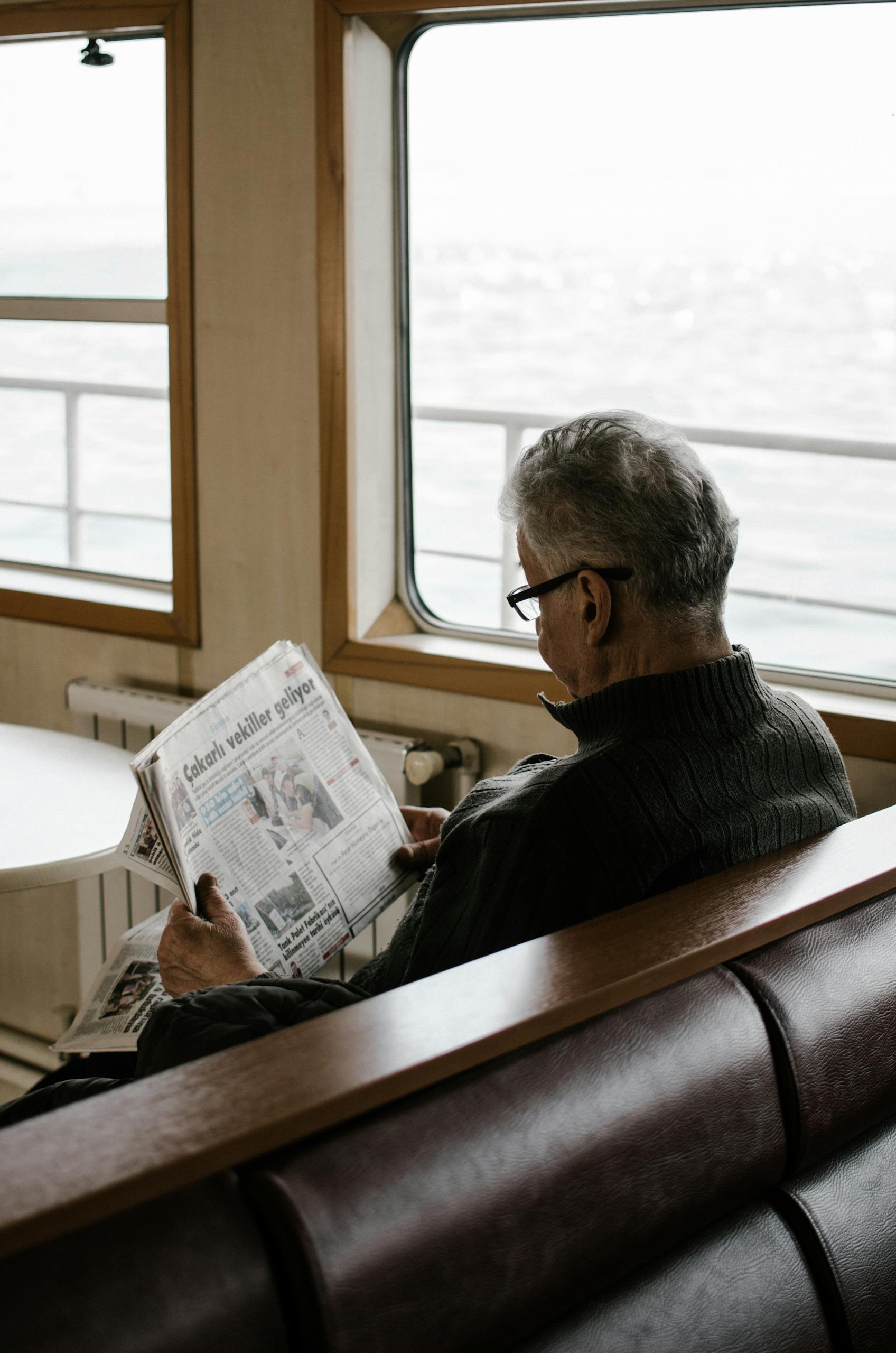 Elderly man reading newspaper inside ferry, enjoying a peaceful travel moment.